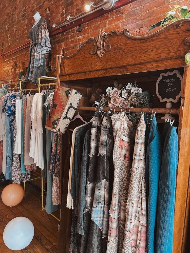 Boutique clothing racks with dresses and tops against an exposed brick wall